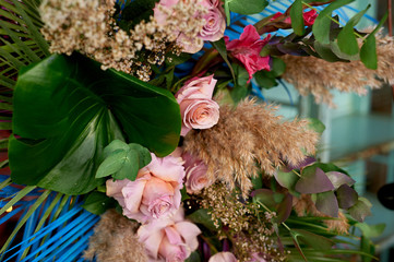 Composition of pampas grass, palm trees and roses. Decorative floral design. The palm tree is painted blue.