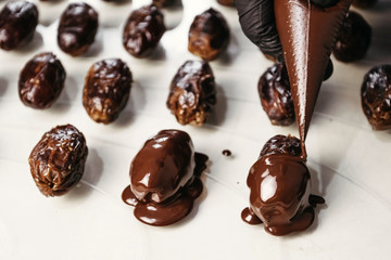Dates in chocolate, dessert. Confectioner pours chocolate over dessert.