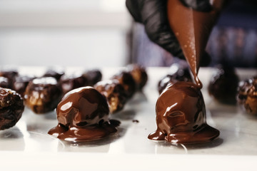 Dates in chocolate, dessert. Confectioner pours chocolate over dessert. Macro, close-up.