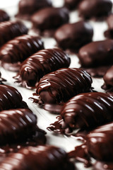 Dates in chocolate, dessert. Confectioner pours chocolate over dessert. Vertical photo.