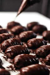 Dates in chocolate, dessert. Confectioner pours chocolate over dessert. Vertical photo.