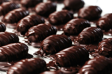 Dates in chocolate, dessert. Confectioner pours chocolate over dessert. Macro, close-up.