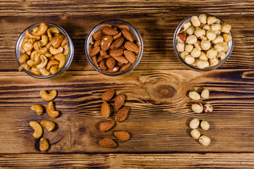 Various nuts (almond, cashew, hazelnut) in glass bowls on a wooden table. Vegetarian meal. Healthy eating concept. Top view