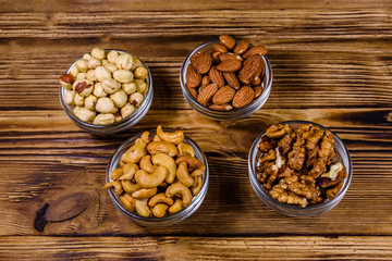 Various nuts (almond, cashew, hazelnut, walnut) in glass bowls on a wooden table. Vegetarian meal. Healthy eating concept