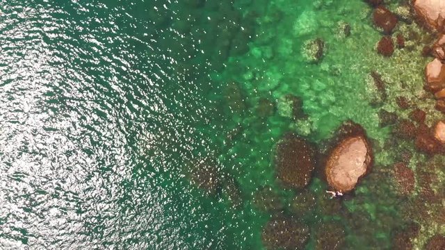 Aerial drone birdseye view shot of woman swimming among the stones on water surface of ocean sea, crystal clear see through turquoise waves, relaxed and chill vacation holiday deserved time
