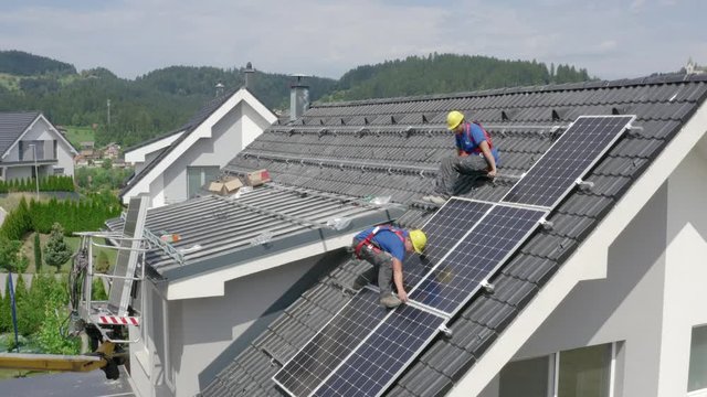 Slow and steady closing in shot of two guys in blue shirts working on rooftop in residential area - fighting against the climate change mounting solar panels