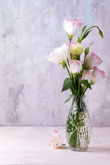 Eustoma flowers in vase on table near stone wall, space for text. Blank for postcards