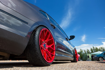 Gray car with lowered suspension and bright red forged wheels is on the parking. Against blue sky