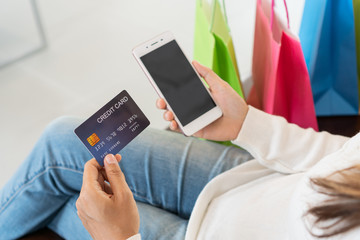 Young woman is relaxing on comfortable couch holding credit card and mobile for online shopping sitting at home. .