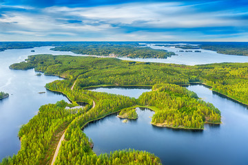 Aerial view of road between green summer forest and blue lake in Finland - obrazy, fototapety, plakaty