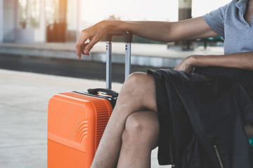 Woman with orange suitcase luggage bag, sitting in train station. Travel concept.