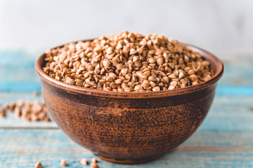 Uncooked buckwheat in a bowl on old boards. Buckwheat is used for cooking.