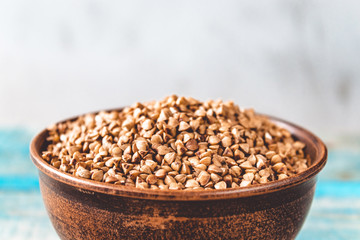 Uncooked buckwheat in a bowl on old boards. Buckwheat is used for cooking.