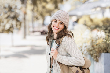 Beautiful joyful woman autumn portrait. Smiling student girl wearing warm clothes and hat in a city in winter