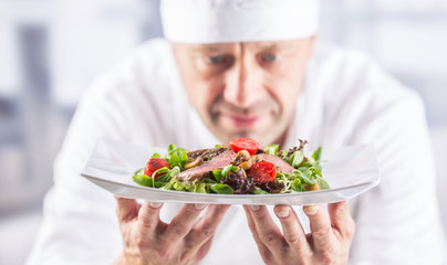 Chef in the kitchen of the hotel or restaurant holding plate with food before serving