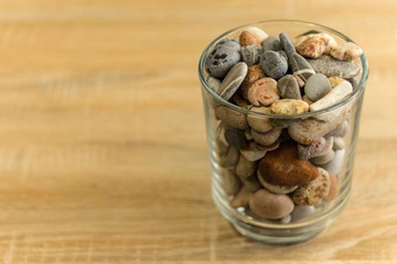 Small sea stones in a glass vessel. The idea of decorating the house with small rocks in a jar on a wooden blurred background.