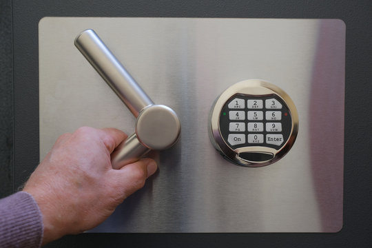 The man's hand opens the armored door of the safe with a digital code lock.