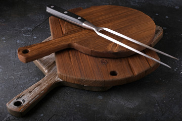 A large meat fork and cutting kitchen boards on a dark table.