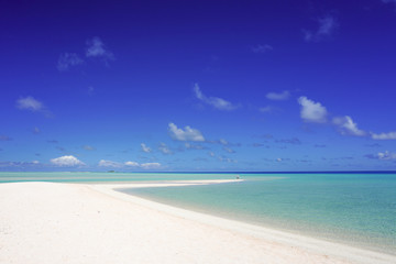 A man looks out over a tropical turquoise lagoon from a white sandy beach under a blue sky with copy space