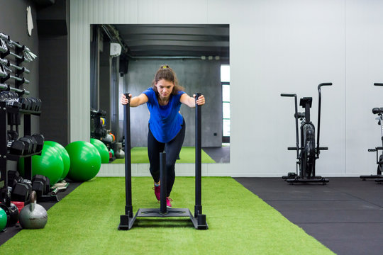Young female fitness trainer performing sled push in local gym.