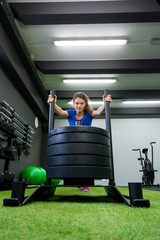 Young female fitness trainer performing sled push in local gym.