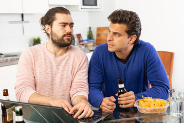 Friendly male meeting over beer at home, men looking at laptop and discussing