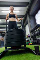 Young female fitness trainer performing sled push in local gym.