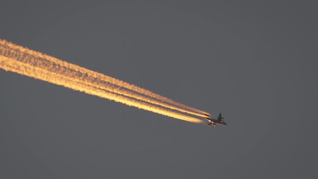 Large airliner with four engines flying above with contrail glowing at dusk