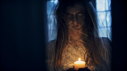 Dead bride with a candle in hand in an abandoned house at night.