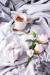 Having a cup of coffee with chocolate, flowers eustoma and gift box on blanket in bed. Holiday concept