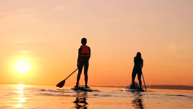 Sunset waters with a boy and a mother doing paddlesurfing
