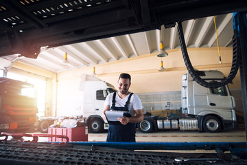 Cheerful truck mechanic doing paperwork before vehicle service in workshop.