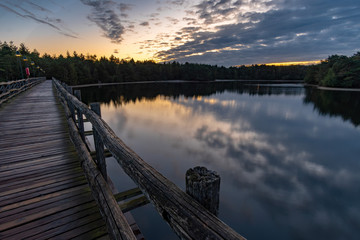 Obraz premium Brücke über einen See mit Wolken bei Sonnenaufgang im Center Parcs De Vossemeren Belgien
