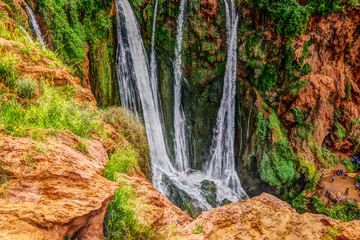 Landscape view of waterfall surrounded with green grass and orang colour terrain, Ouzoud Falls. Moyen Atlas village of Tanaghmeilt, Atlas mountains, Morocco.