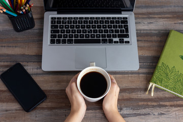Flat lay workspace desk top view: laptop keyboard, phone, notebook and cup of coffee in hands. Coffee break!