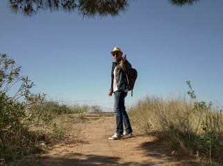 A man traveler in a hat and with a backpack stands on the observation deck of a hill and holds out his hand