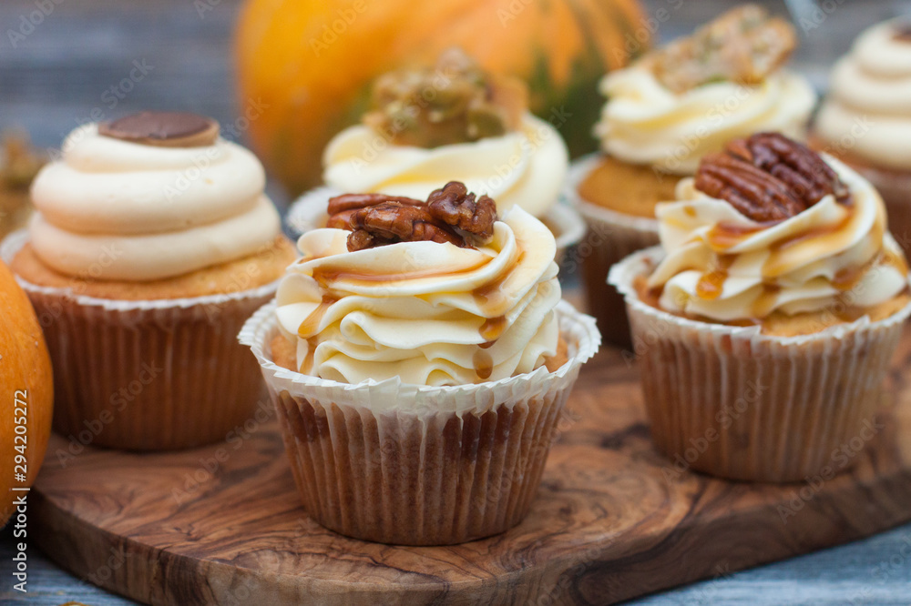 Wall mural pumpkin cupcakes with cream cheese frosting decorated with pecan nuts, maple syrup, caramel bites an