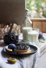 Bread toast with plum jam, served with milk and plums on a wooden background. Rustic style.