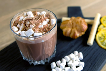 Cocoa with marshmallow in rock glass on a wood black tray with cake and lemon. Close-up view