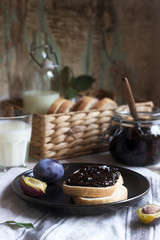 Bread toast with plum jam, served with milk and plums on a wooden background. Rustic style.