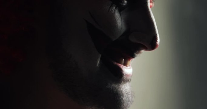 Jester with wicked frightening humor. Evil smile on frightening face of scary clown in dark at halloween, mouth closeup. Terrible horror makeup for the traditional celebration halloween holiday.
