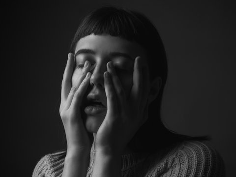 Sad young woman with hands on face. Black and white. Close up
