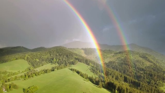 Beautiful double rainbow moving over fresh green forest landscape in sunny summer evening after rain Aerial