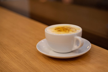 Hot art latte coffee in a white cup with a saucer on wooden table. Coffee shop blur background with bokeh image. Coffee lovers concept