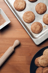 Snickerdoodles or sugar cookies on a baking tray and a plate on wood table with a bowl full of sugar and cinnamon and a rolling pin. Vertical Shot