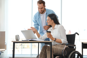 Young woman in wheelchair with colleague at workplace