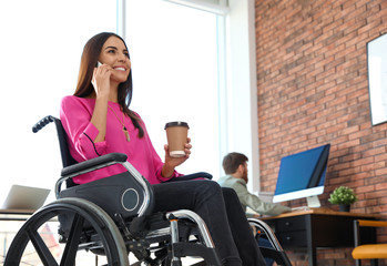Young woman in wheelchair talking on smartphone at office