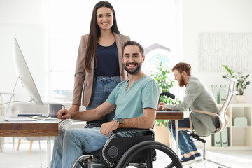 Young man in wheelchair with colleagues at workplace