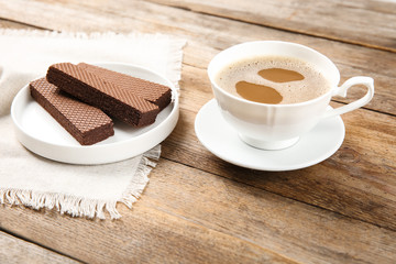 Plate of delicious chocolate wafers with cup of coffee on brown wooden background