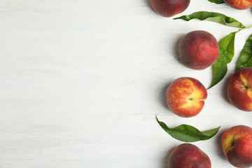 Fresh peaches and leaves on white wooden table, flat lay. Space for text